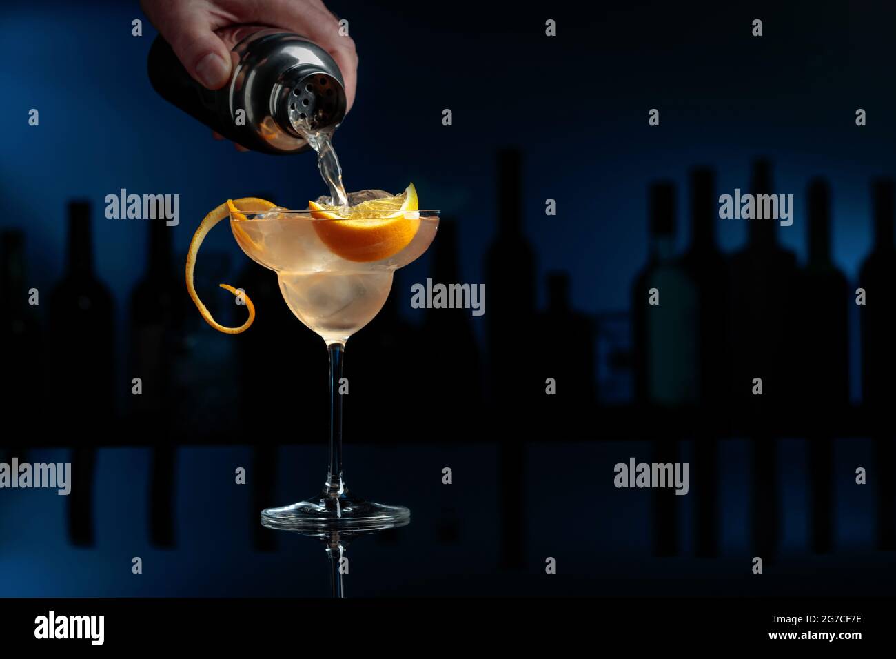 Cocktail « Great Gatsby » sur fond noir réfléchissant. Le barman verse un cocktail d'un shaker dans un verre avec de la glace. Banque D'Images
