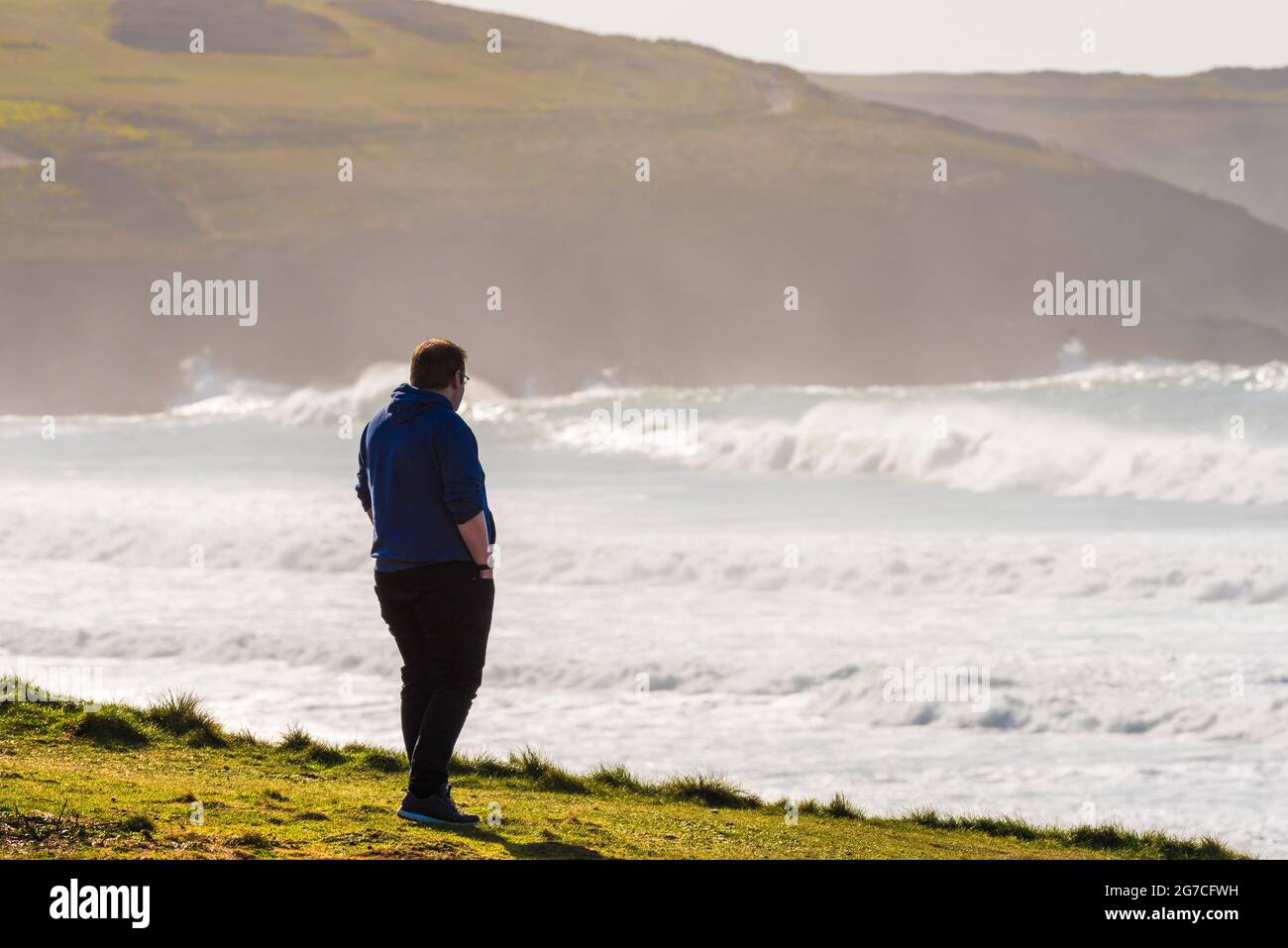 Un homme debout sur le sentier côtier qui regarde au-dessus de la baie de Fistral à Newquay, en Cornouailles. Banque D'Images