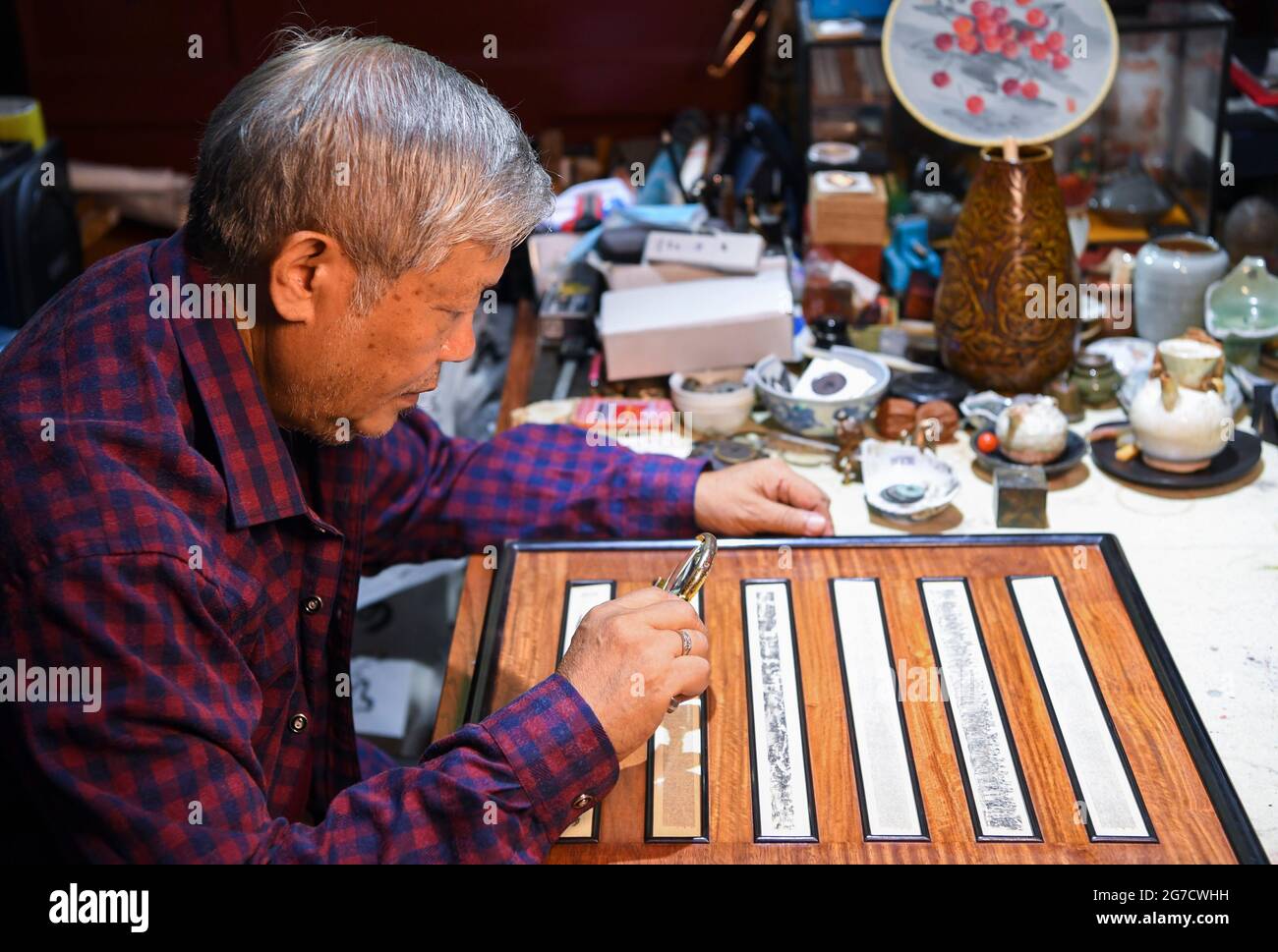 (210713) -- CHONGQING, le 13 juillet 2021 (Xinhua) -- Pan Qihui vérifie ses œuvres miniatures dans son studio à Chongqing, dans le sud-ouest de la Chine, le 12 juillet 2021. PAN Qihui, 72 ans, un héritier avec plus de 40 ans d'expérience dans la sculpture miniature qui emploie des matériaux comme l'or, jade, la porcelaine même les cheveux pour créer des mini-œuvres exquises. PAN aime la calligraphie et la peinture depuis son enfance, et a commencé à être enthousiaste au sujet de la sculpture miniature dans les années 1980. Il a appris l'art des maîtres et en raison du manque de matériaux, il a pratiqué la technique sur les brosses à dents et les baguettes au début. En 2018, il Banque D'Images