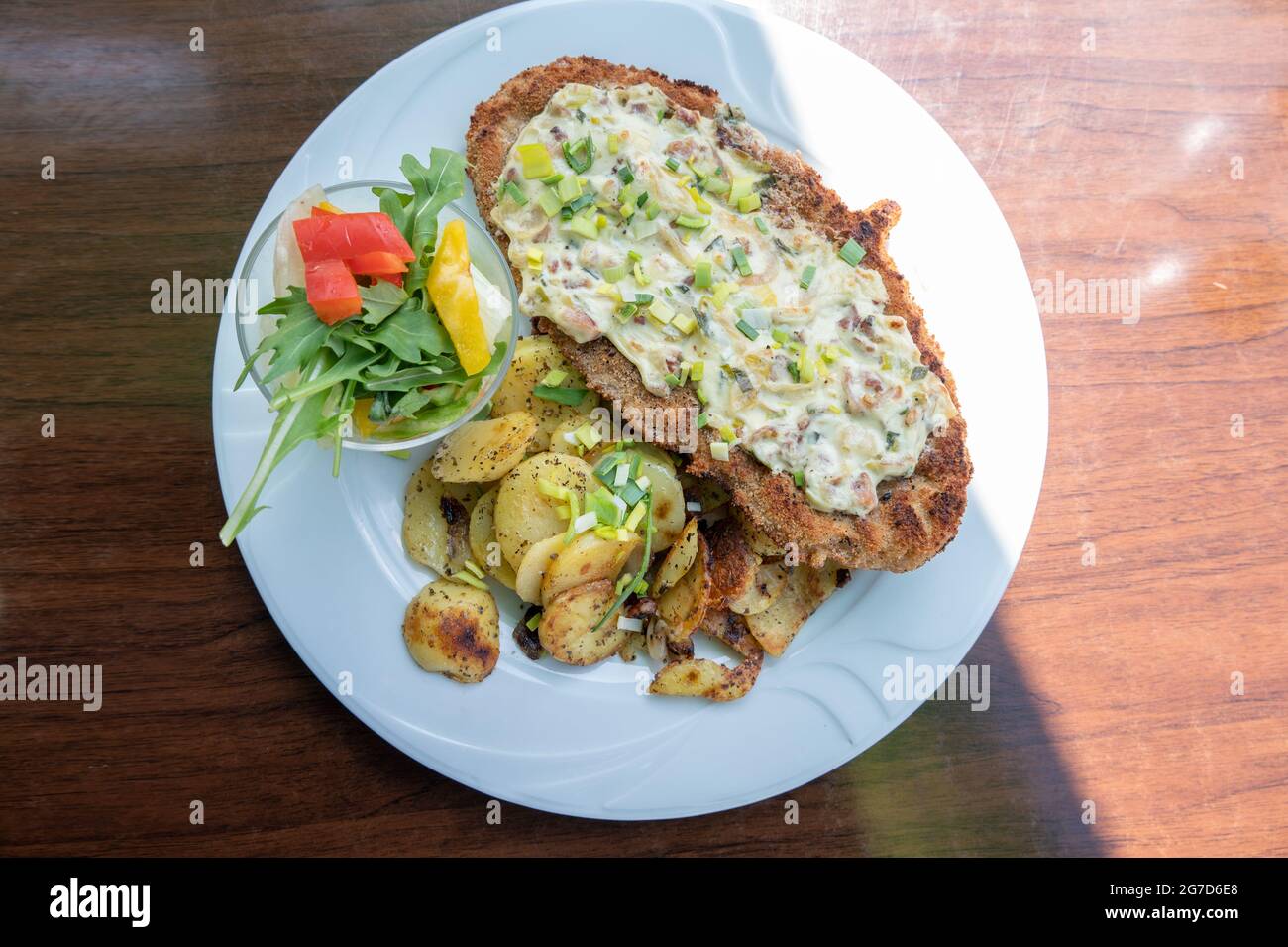 Schnitzel pané avec sauce au fromage, pommes de terre frites et salade sur une assiette blanche et une table en bois marron, vue d'en haut, sélection Banque D'Images