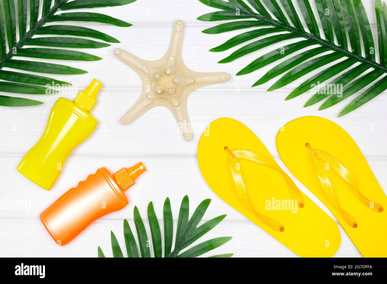 Été mer vacances concept créatif. Crème solaire en spray, sandales à rabat, étoiles de mer aux feuilles de palmier tropicales sur des panneaux de bois blancs. Vue de dessus Banque D'Images