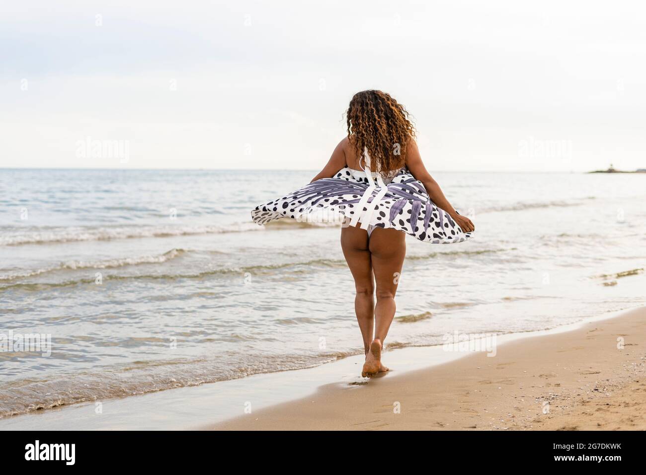 Femme marchant le long de la plage de sable au coucher du soleil.Femme appréciant les vacances d'été jouant et dansant avec pareo élégant sur le bord de mer. Banque D'Images