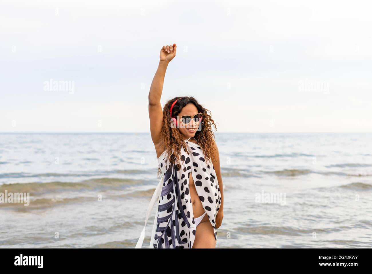 Joyeux jeune belle afro-américaine femme souriante, portant des écouteurs dansant et levant le bras. Banque D'Images