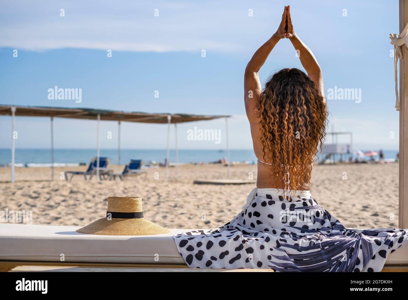 Vue arrière portrait de cheveux bouclés méconnaissables femme avec les bras levés , pose de yoga , assis sur un banc sur la plage paysage.Relax vacances d'été conc Banque D'Images