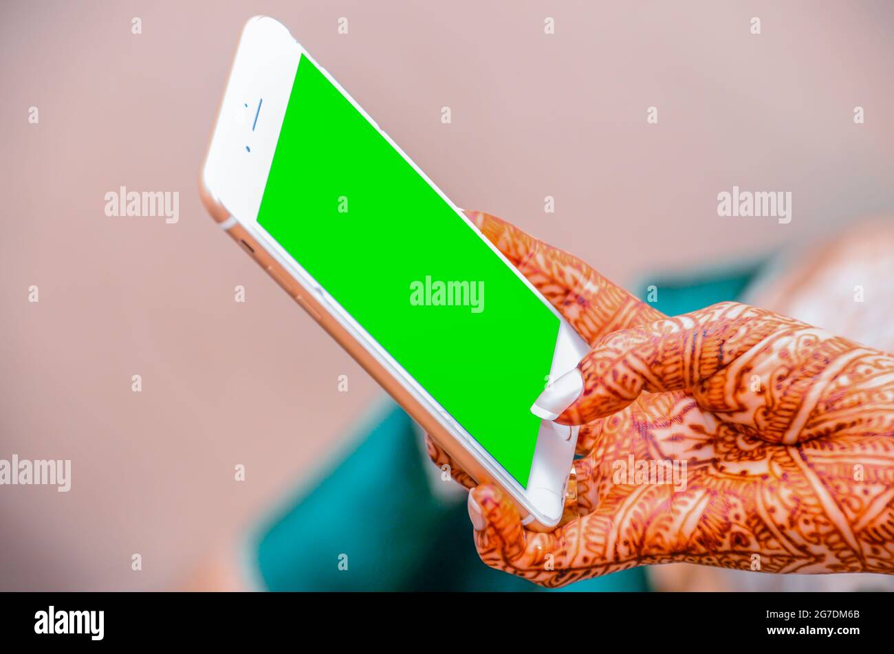 Main d'une mariée tatouée avec henné tenant un téléphone avec un écran vert Banque D'Images