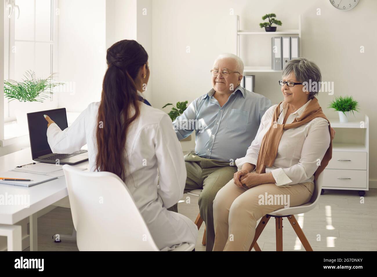 Heureux couple d'âge mûr et leur médecin communiquant tout en utilisant l'ordinateur portable pendant le rendez-vous médical. Banque D'Images