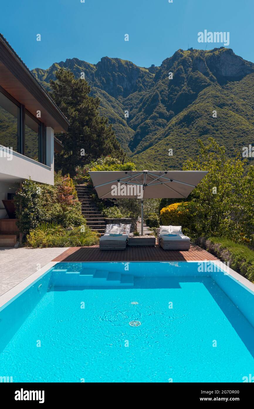 Maison moderne de deux étages avec grande piscine donnant sur les montagnes. Deux chaises longues et un grand parapluie ouvert pour profiter de vos vacances. Personne à l'intérieur Banque D'Images
