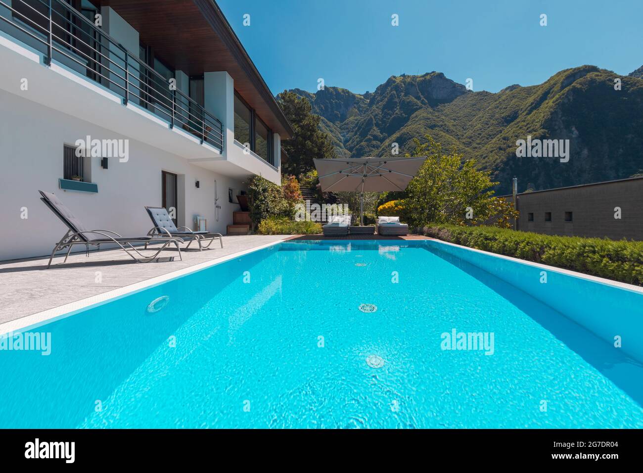 Maison moderne de deux étages avec grande piscine donnant sur les montagnes. Deux chaises longues pour profiter du soleil, deux chaises longues et un grand parasol Banque D'Images