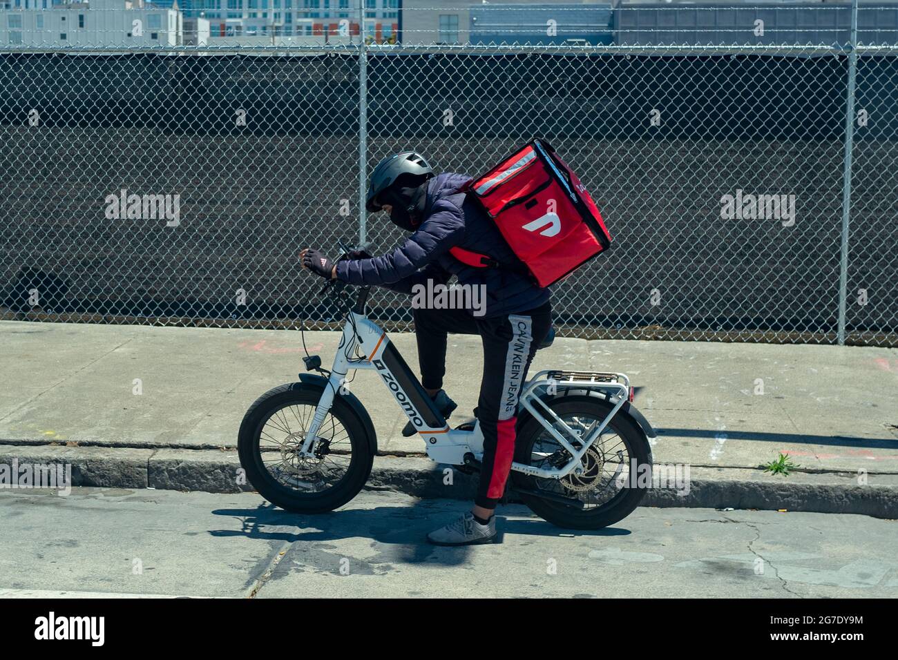 Conducteur de Doordash sur vélo électrique portant un sac à dos plus froid et téléphone de conseil avec horizon de San Francisco, Californie en arrière-plan, le 3 juin 2021. () Banque D'Images