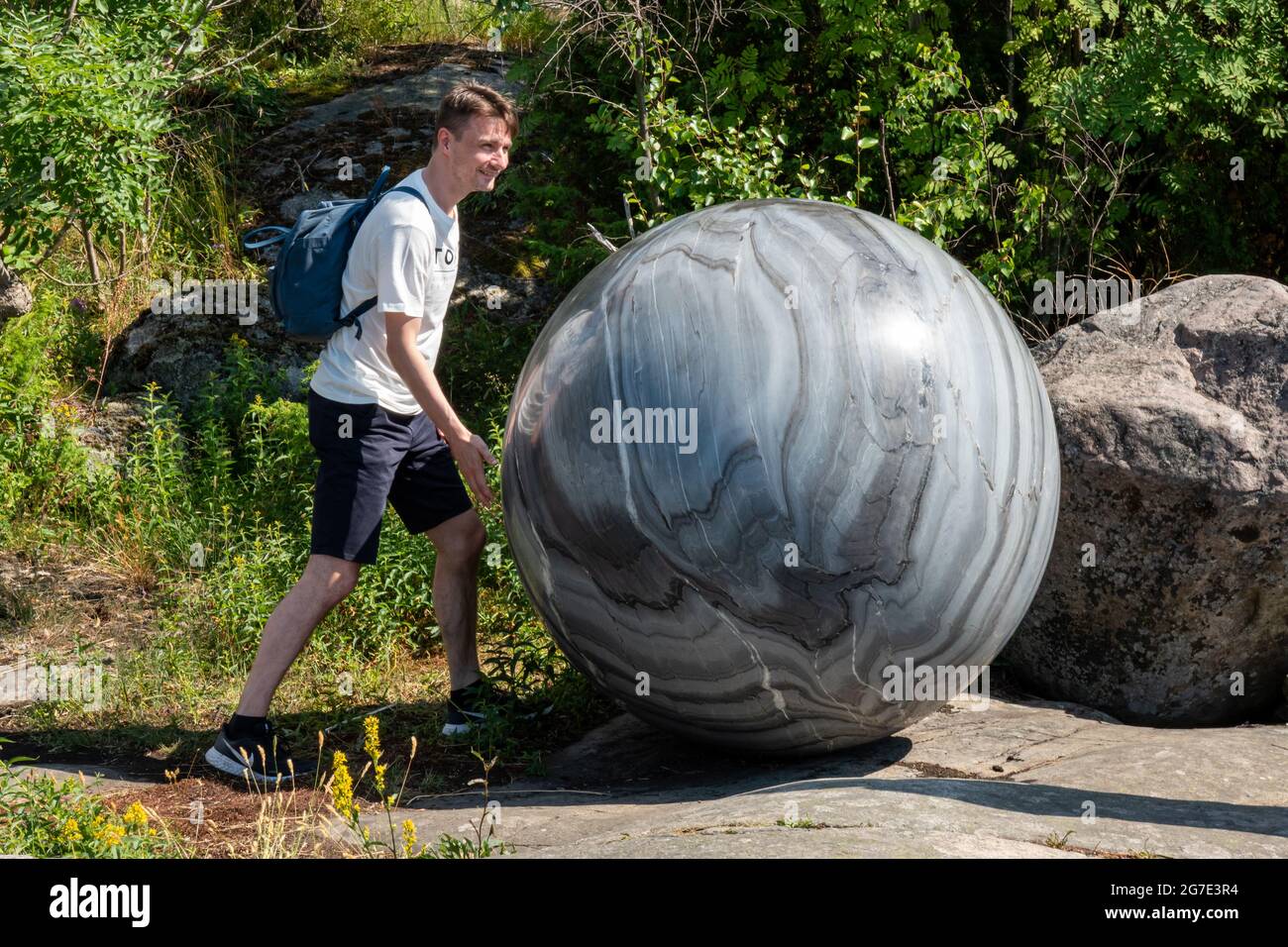 Homme posant avec un globe de pierre, faisant partie de la sculpture de Pars Pro Toto par Alica Kwade, à la Biennale d'Helsinki 2021, sur l'île de Vallisaari, à Helsinki, en Finlande Banque D'Images