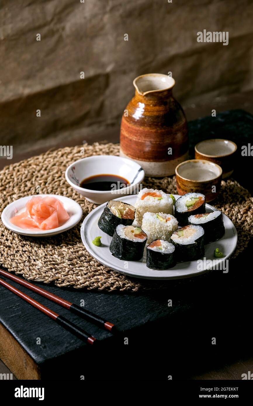 Petits pains à sushis faits maison au saumon, omelette japonaise, avacado, gingembre et sauce soja avec baguettes sur une serviette en paille sur une table en bois de palet. Cerami Banque D'Images