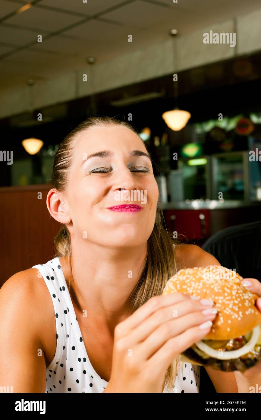 Une femme heureuse dans un restaurant de restauration rapide qui mange un hamburger semble l'apprécier Banque D'Images