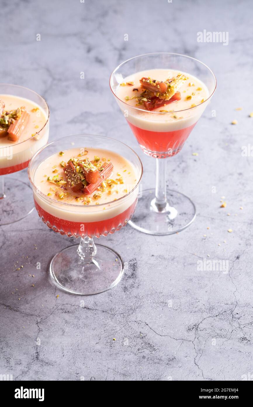 Gelée de rhubarbe et panna cotta servies dans des verres vintage, recouverts de rhubarbe pochée et de pistaches hachées Banque D'Images