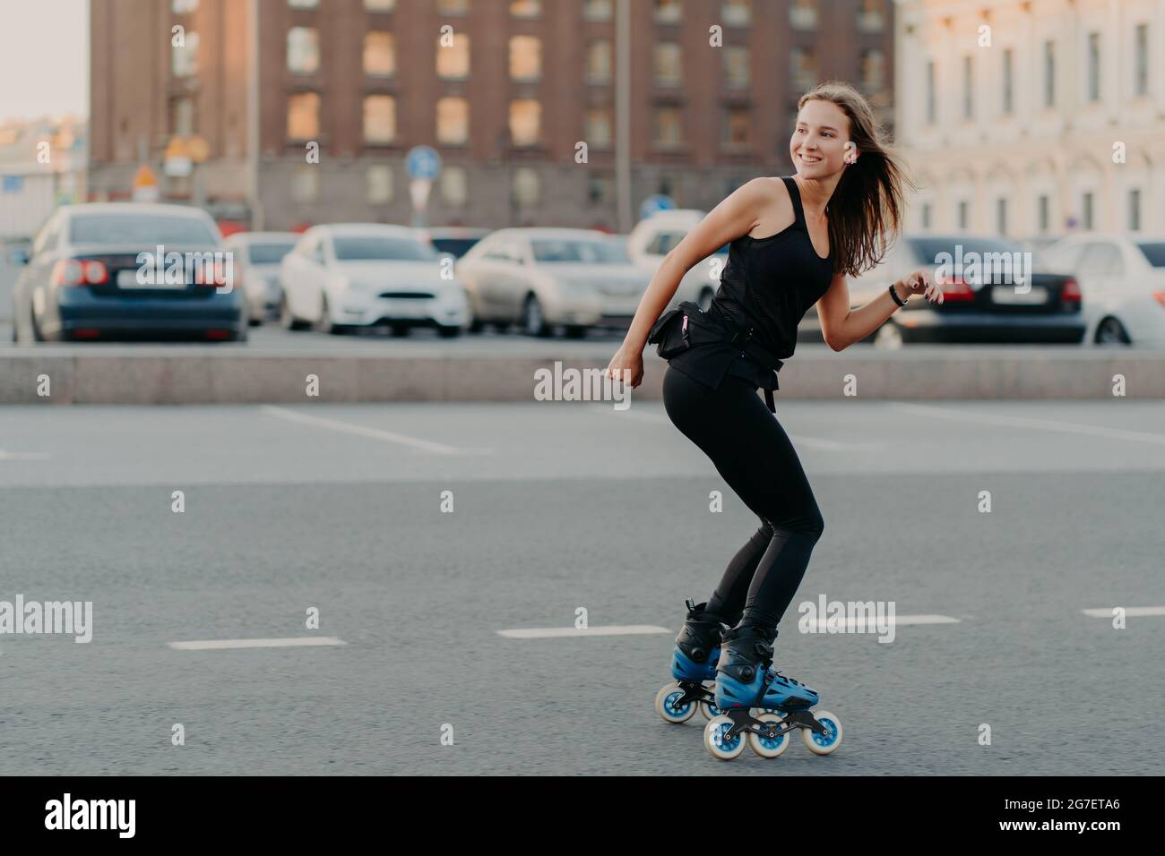 Photo extérieure d'une femme gaie et fine vêtue d'un vêtement actif qui regarde loin mène à des manèges sains sur roulettes pose sur la route dans les sensations d'un endroit urbain Banque D'Images