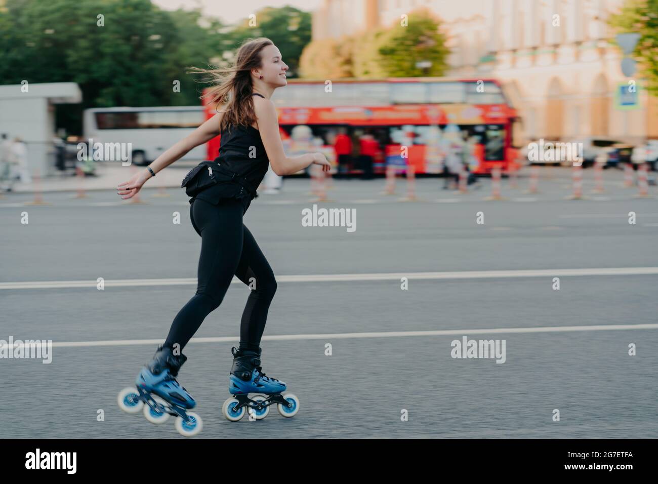 Photo en extérieur d'une jeune femme active mince aime le roller pendant le temps libre vêtu de vêtements de noirceur pose en milieu urbain sur la route contre Banque D'Images