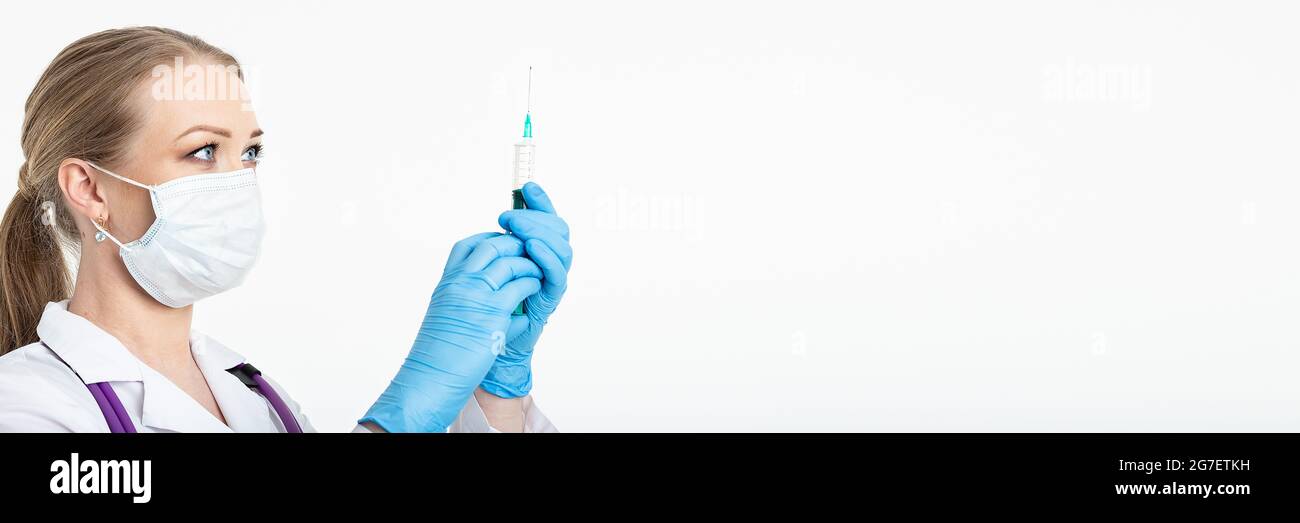 Une jeune infirmière dans un masque compose le vaccin dans une seringue tout en étant assise dans un hôpital à côté d'un patient. Patiente en attente de l'injection de la grippe Banque D'Images