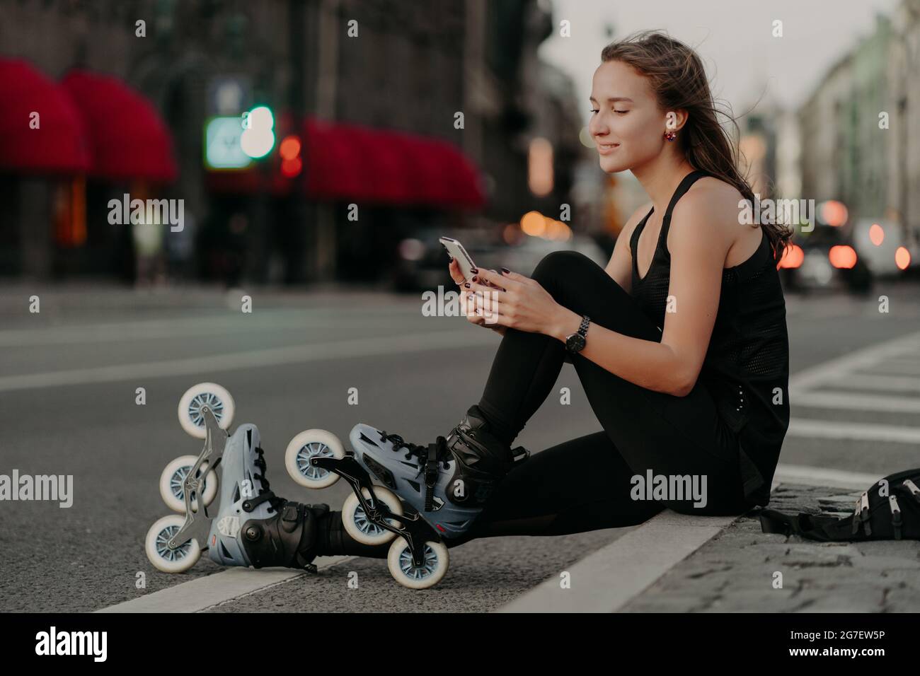 Prise de vue horizontale d'une femme sportive active vêtue de vêtements de  sport porte des rollerblades focalisées sur le smartphone. Elle aime le  patinage en ligne en plein air Photo Stock -