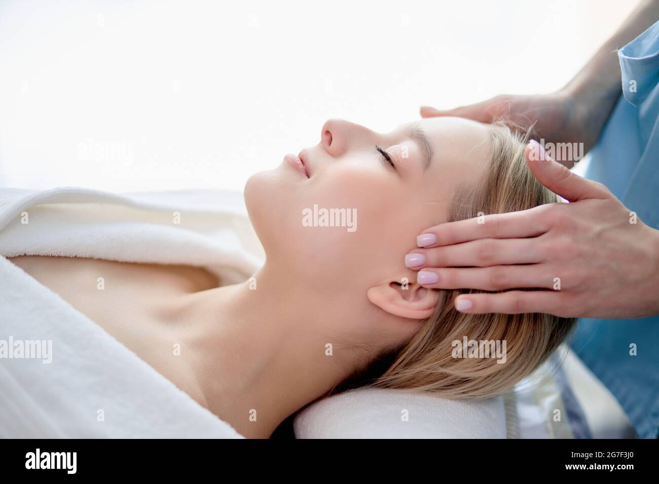 Gros plan portrait vue latérale de blonde calme femme se reposer, se détendre dans le salon de spa, couché avec les yeux fermés, les mains du masseur court sur les temples. Heult Banque D'Images