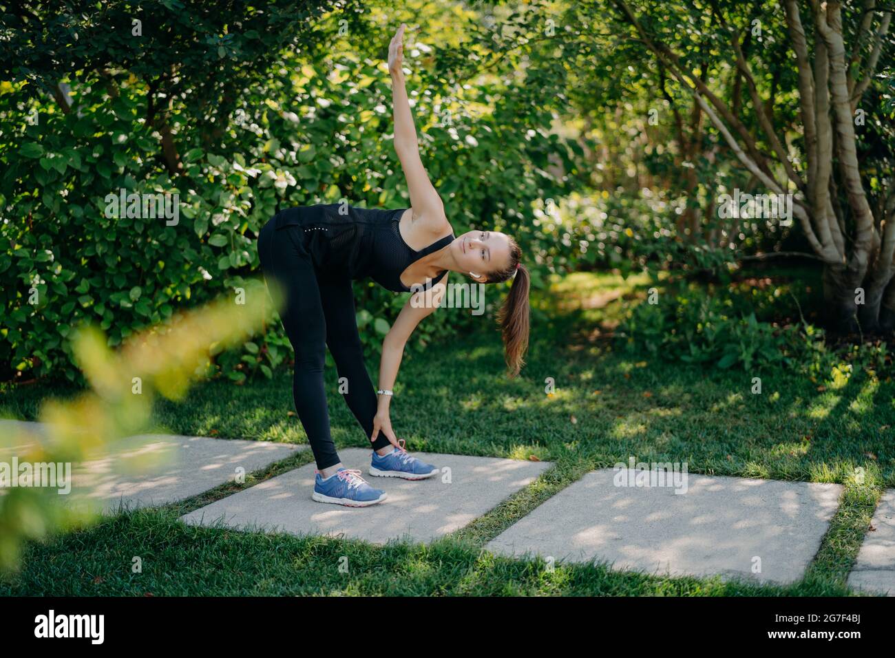 Exercice physique actif modèle d'entraînement en plein air s'incline aux pieds lève le bras prépare les muscles avant les défis d'entraînement cardio elle-même habillée en vêtements actifs a Banque D'Images