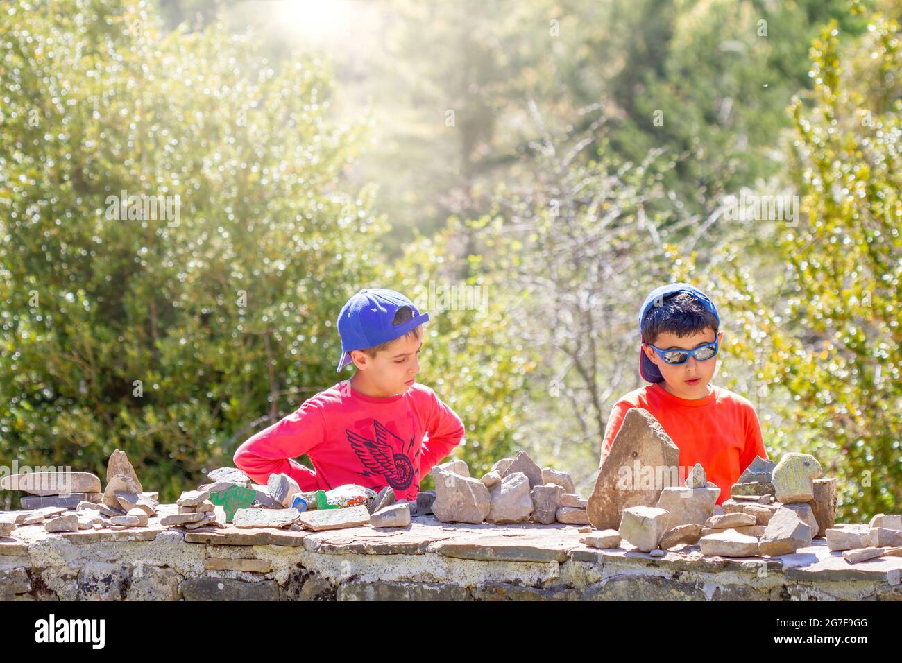 deux garçons font des constructions avec des pierres sur un mur d'ardoise dans un environnement naturel entouré d'arbres et le soleil du soir, à l'horizontale Banque D'Images