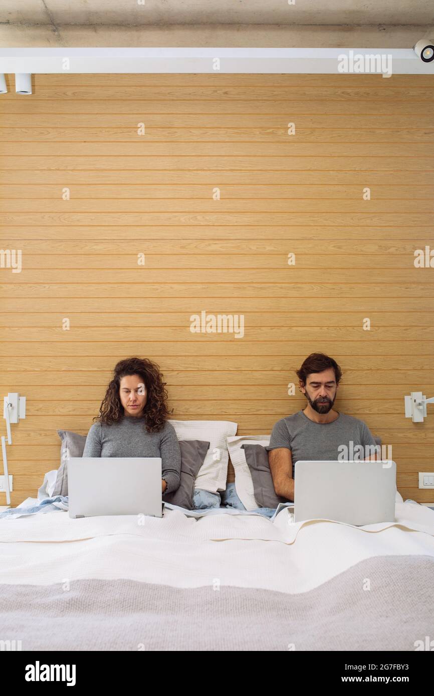Couple dans un lit double king size chacun avec leur ordinateur portable fonctionnant en regardant chacun de leurs écrans. Concept : bureau à domicile Banque D'Images