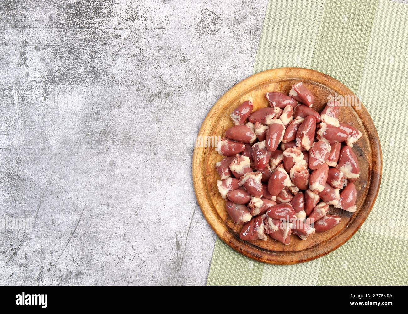 Cœurs de poulet crus sur une planche à découper ronde en bois sur fond gris foncé. Vue de dessus, plan d'appartement Banque D'Images