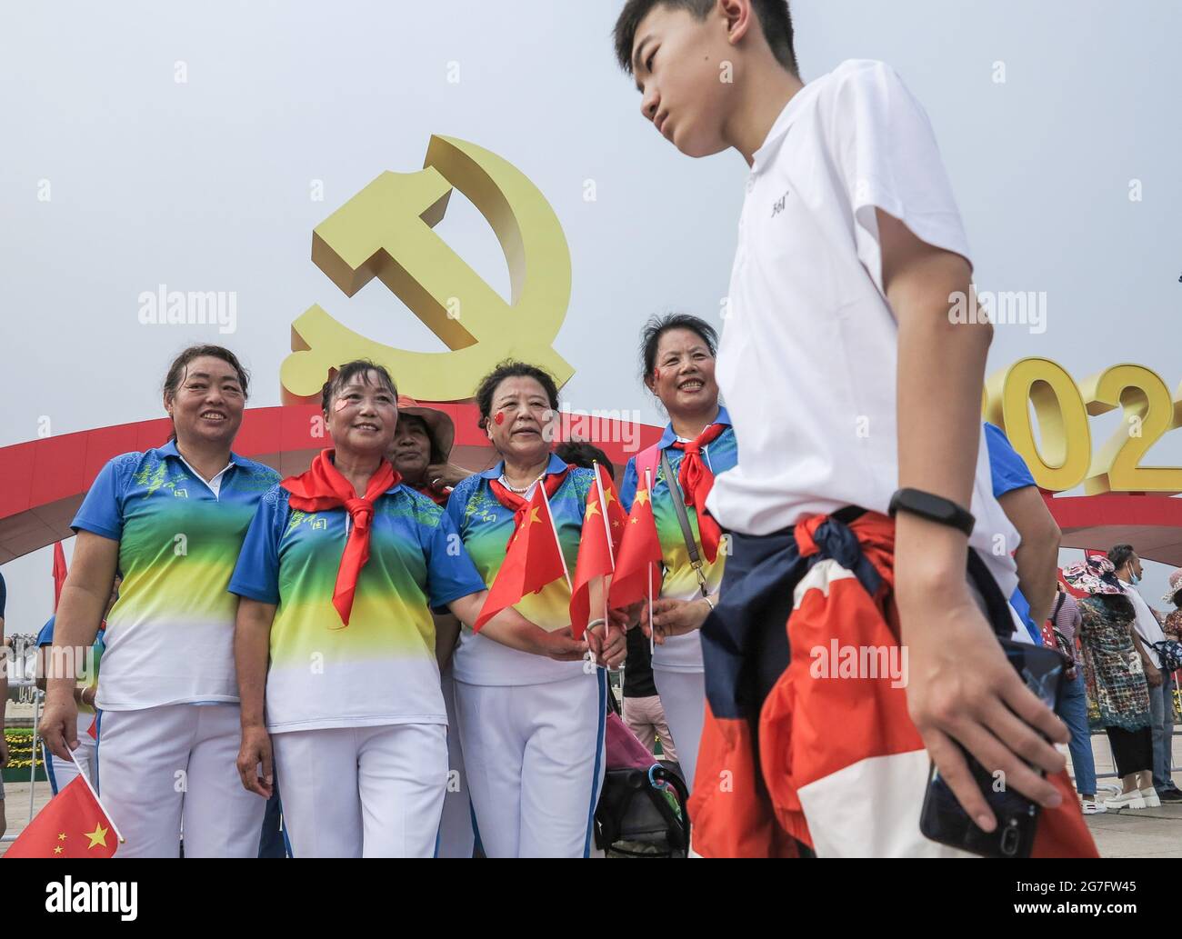 11 juillet 2021, Beijing, Chine : les touristes portant des foulards rouges,  des vêtements uniformes tiennent des drapeaux nationaux tout en prenant des  photos sous l'emblème du Parti communiste sur la place