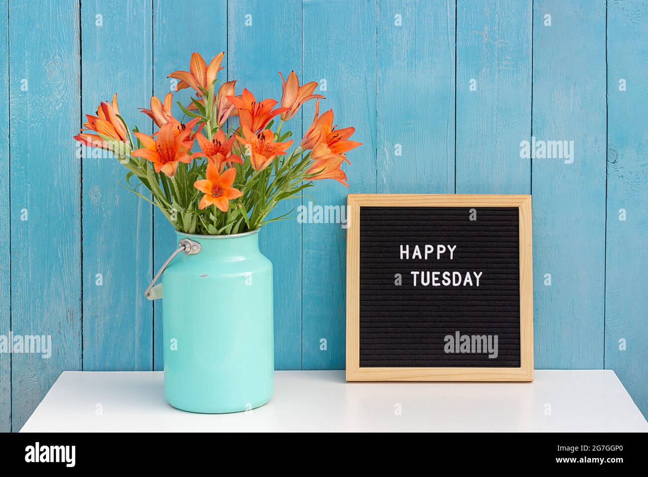 Happy Tuesday mots sur le tableau noir de lettres et bouquet de fleurs orange sur la table contre le mur en bois bleu. Concept Bonjour mardi. Banque D'Images
