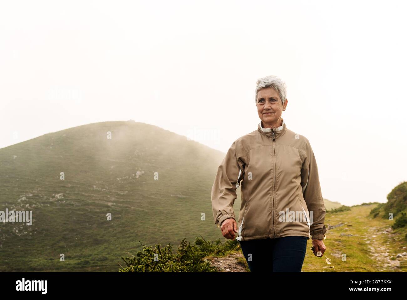 Voyageur âgé avec de courts cheveux gris qui regarde loin et marche sur le sentier près de la colline en journée dans la nature Banque D'Images