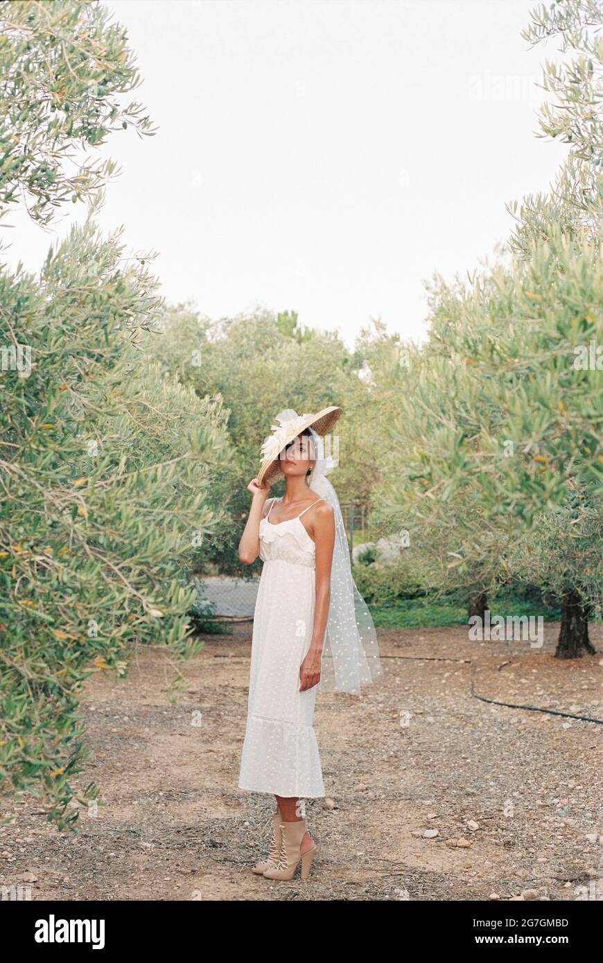 Vue latérale de l'élégante mariée en robe blanche et chapeau de paille  debout dans le jardin en campagne et regardant l'appareil photo Photo Stock  - Alamy