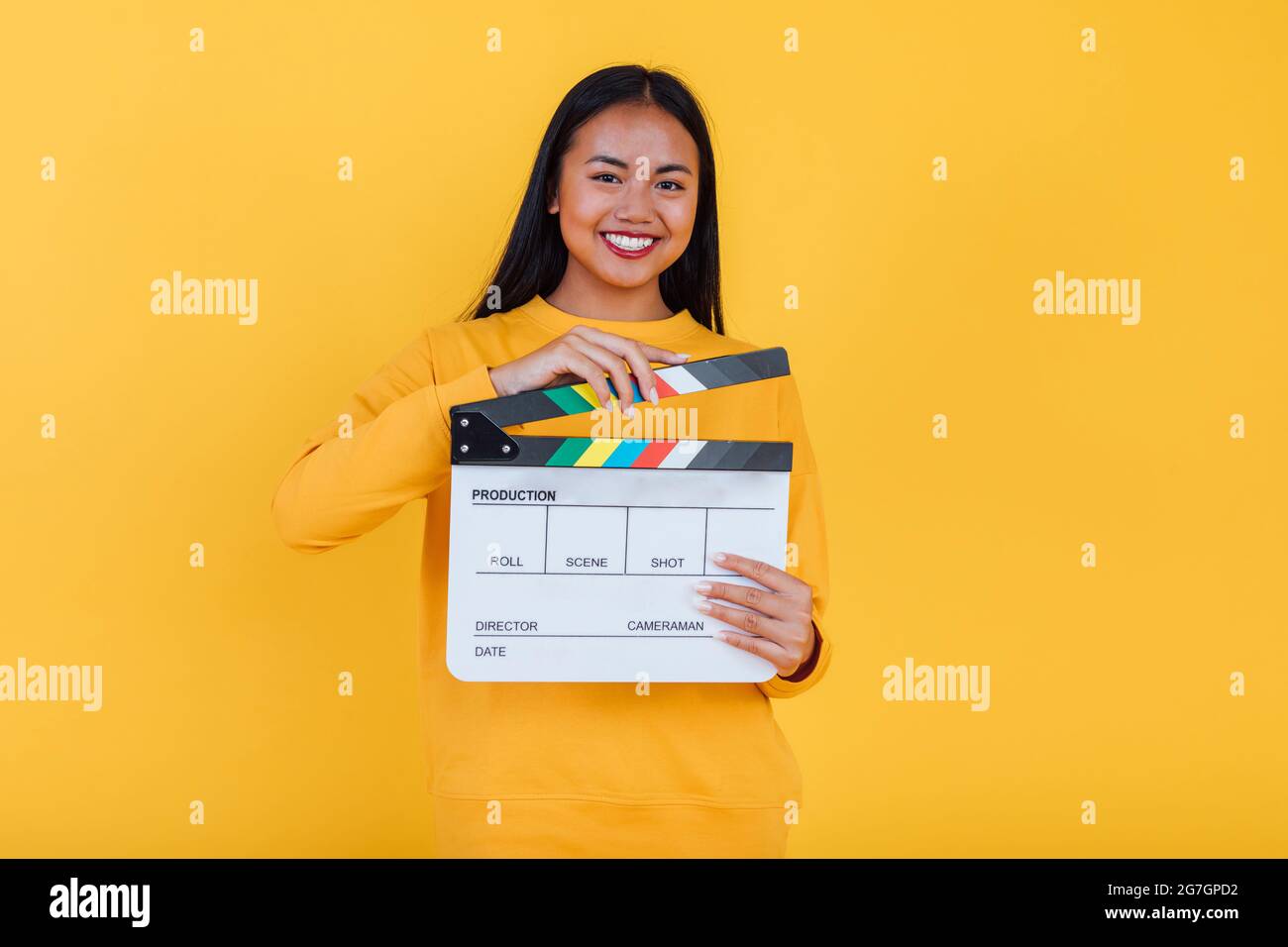 Femme ethnique gaie debout avec le film clapper sur fond jaune en studio et regardant la caméra Banque D'Images