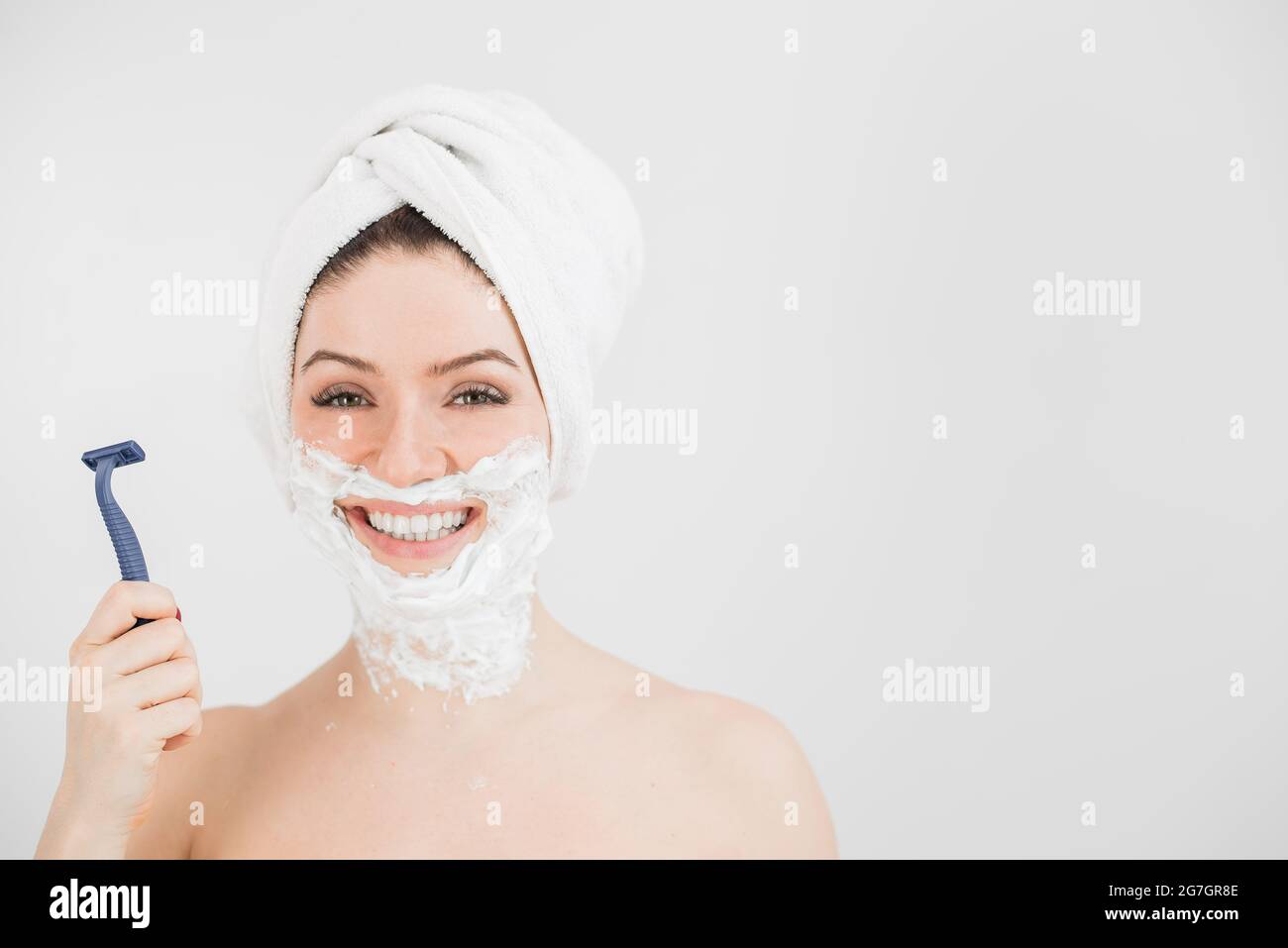Gaie femme caucasienne avec une serviette sur sa tête et la mousse de rasage  sur son visage tient un rasoir sur un arrière-plan blanc Photo Stock - Alamy