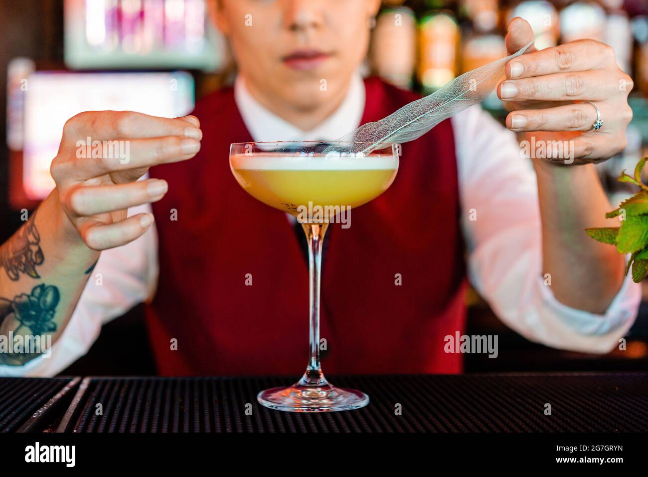 Anonyme professionnelle jeune femme barman décorant avec une plume tout en préparant le cocktail aigre au bar Banque D'Images