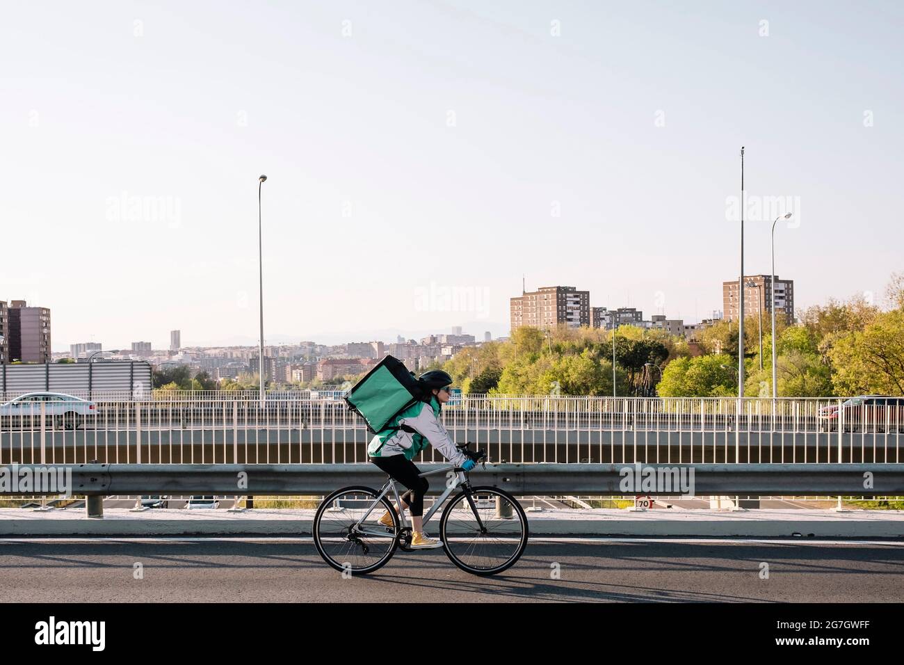 Vue latérale d'une coursier féminine avec sac thermique sur le pont en vélo tout en livrant de la nourriture en ville, espace de copie ci-dessus Banque D'Images