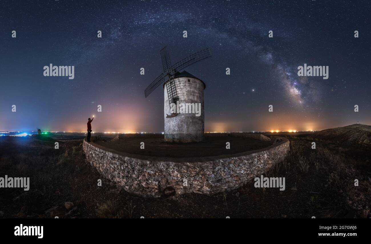 Paysage pittoresque de la voie lactée dans un ciel sombre de nuit au-dessus de la tour du moulin à vent en pierre avec des lumières lumineuses à distance Banque D'Images