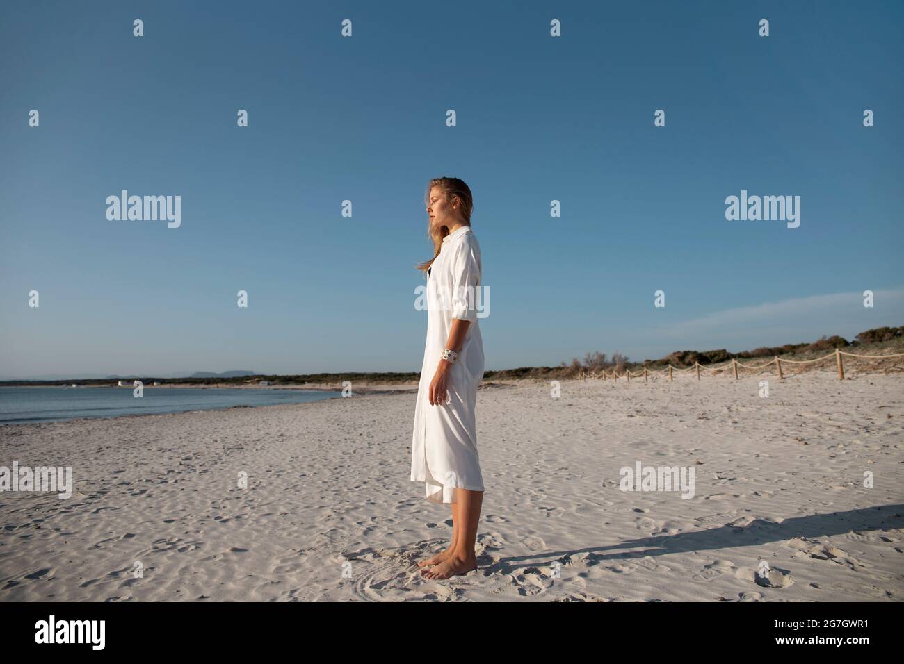 Femme blonde aux cheveux longs se tenant sur la plage en regardant au loin Banque D'Images