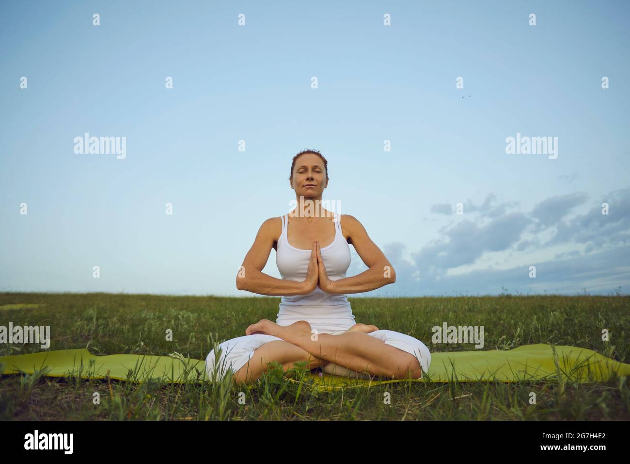 Femme adulte assise en position Lotus avec les yeux fermés et les mains jointes à Namaste Banque D'Images