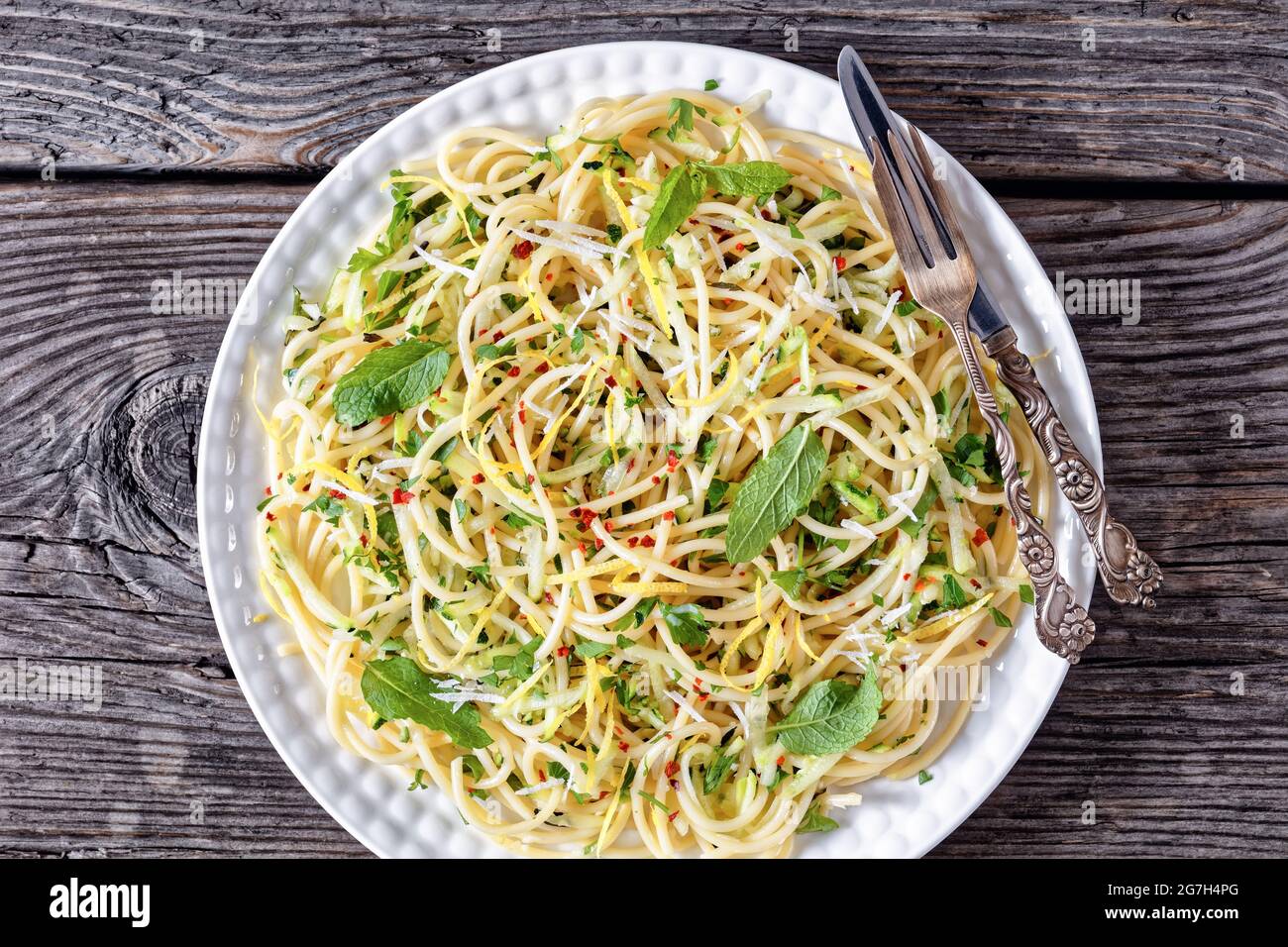 spaghetti d'été alla carrettiera avec feuilles de menthe, zeste de citron, fromage pecorino, piments de flocons, persil et courgettes râpées sur une assiette blanche Banque D'Images