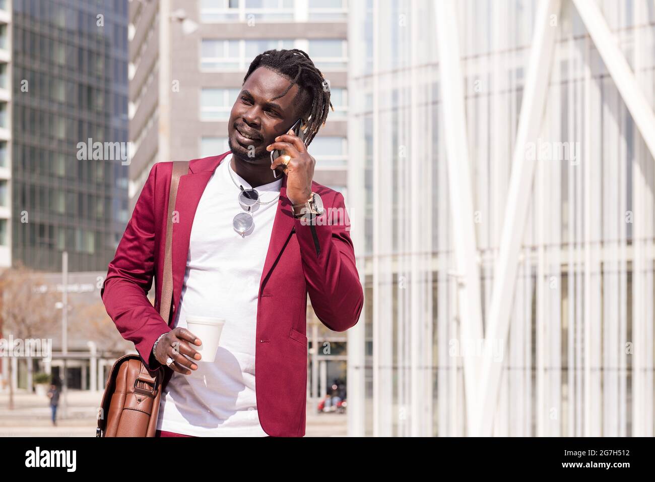 homme d'affaires africain élégant marchant dans le centre financier de la ville parlant au téléphone avec un café dans sa main, concept de la technologie et de comm Banque D'Images