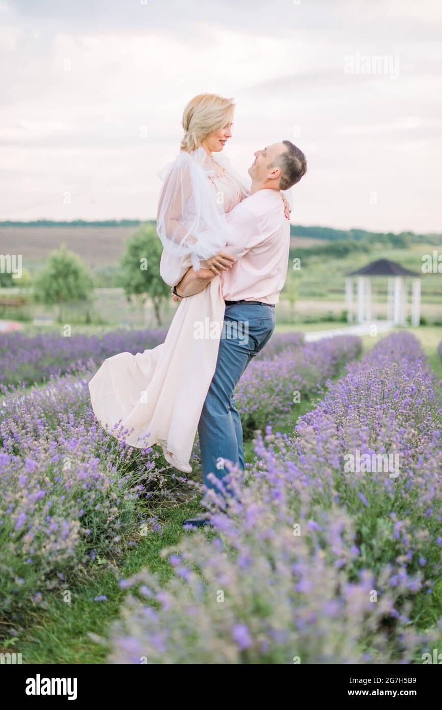 Joyeux Couple D Age Moyen Dans Le Champ De Fleurs De Lavande Pourpre Ont Un Moment Romantique Et Celebration D Anniversaire De Mariage L Homme Tient Sa Femme Sur Les Mains Et Danse Photo Stock