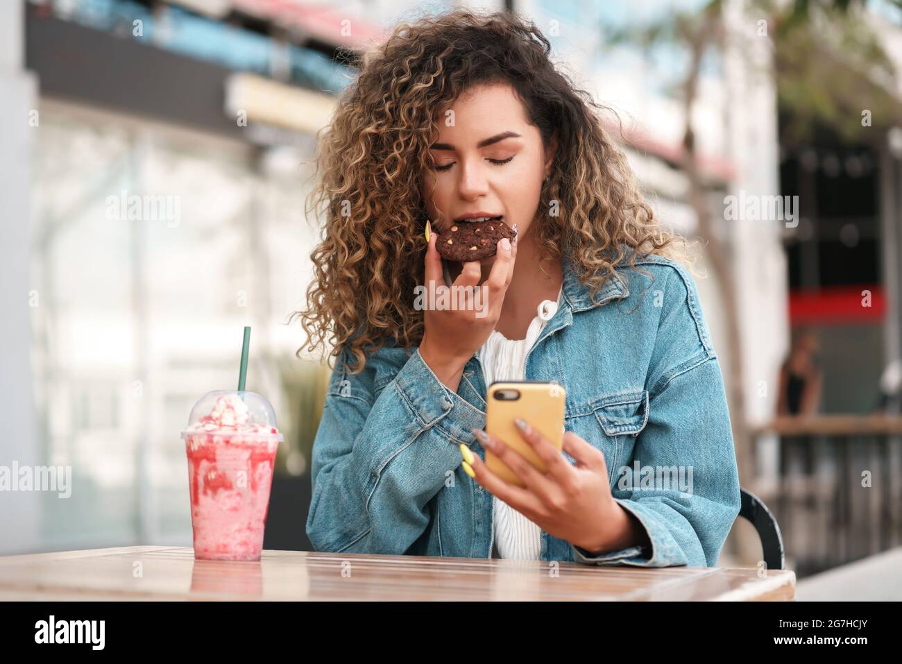Femme latine utilisant un téléphone portable tout en étant assise dans un café. Banque D'Images