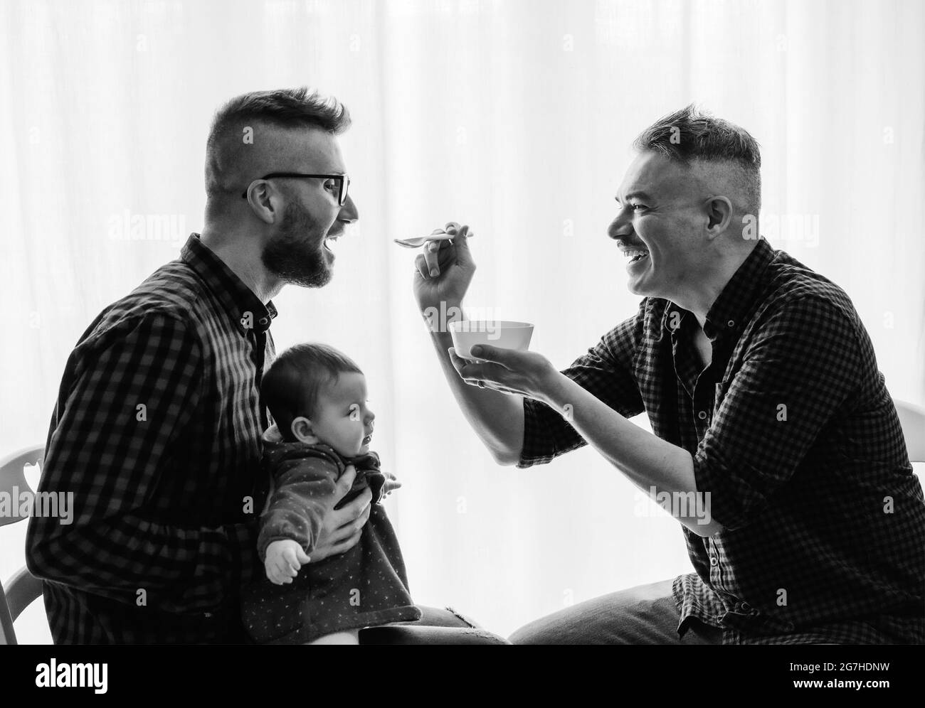 Homme gay couple avec adopté bébé fille à la maison - Deux beaux pères nourrissent la petite fille dans la cuisine - Baby-sitters masculins - famille LGBT à la maison - diversité Banque D'Images