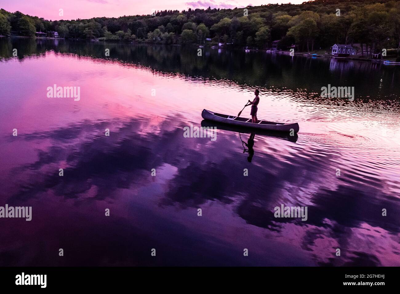 Le canoéiste se dresse en canoë tout en pagayant sur un petit lac près de Cooperstown, NY, au coucher du soleil. Banque D'Images