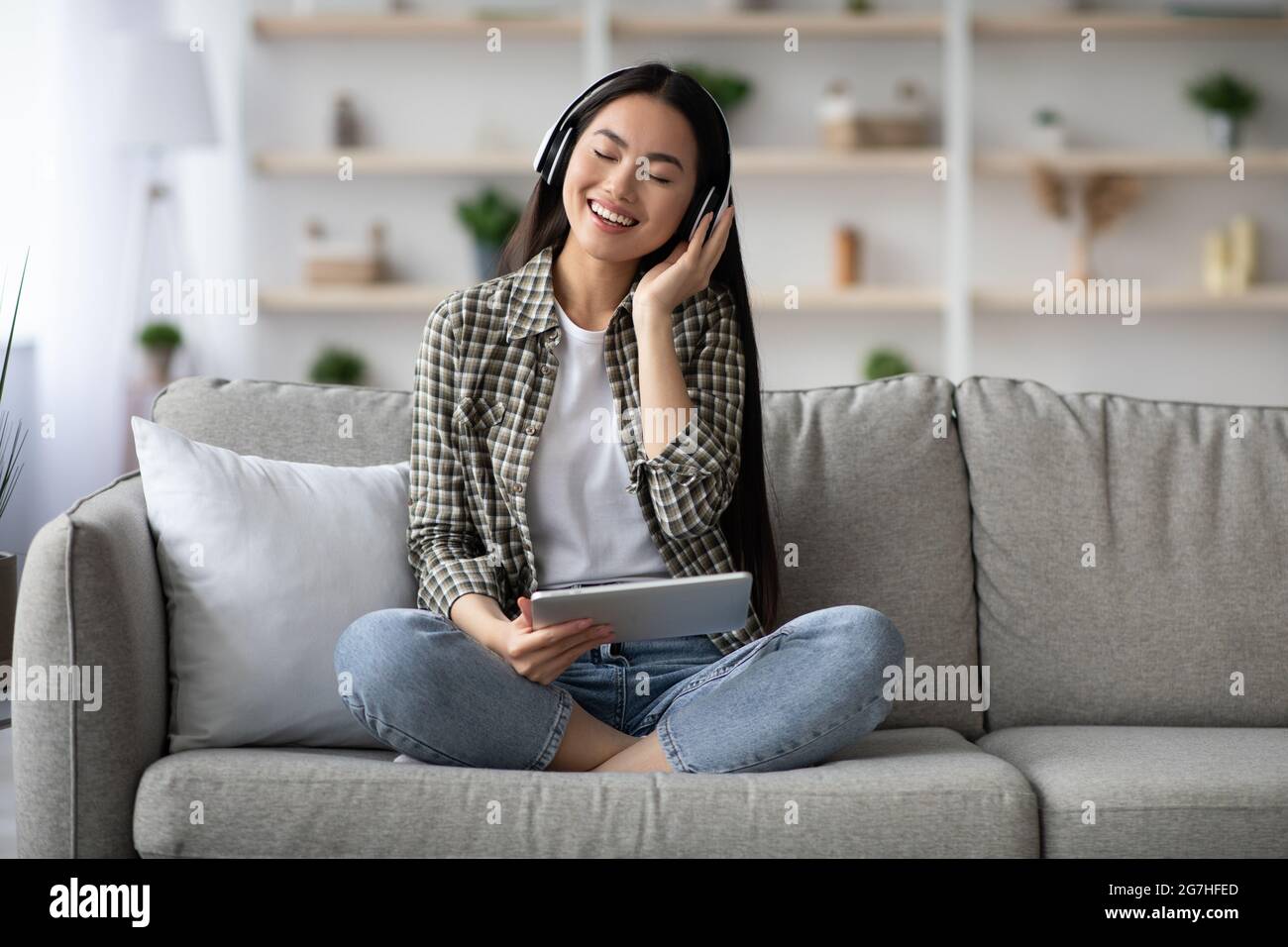 Joyeuse jeune femme asiatique écoutant de la musique en ligne, en utilisant un casque stéréo sans fil et une nouvelle application mobile sur tablette numérique, femme chinoise sitti Banque D'Images