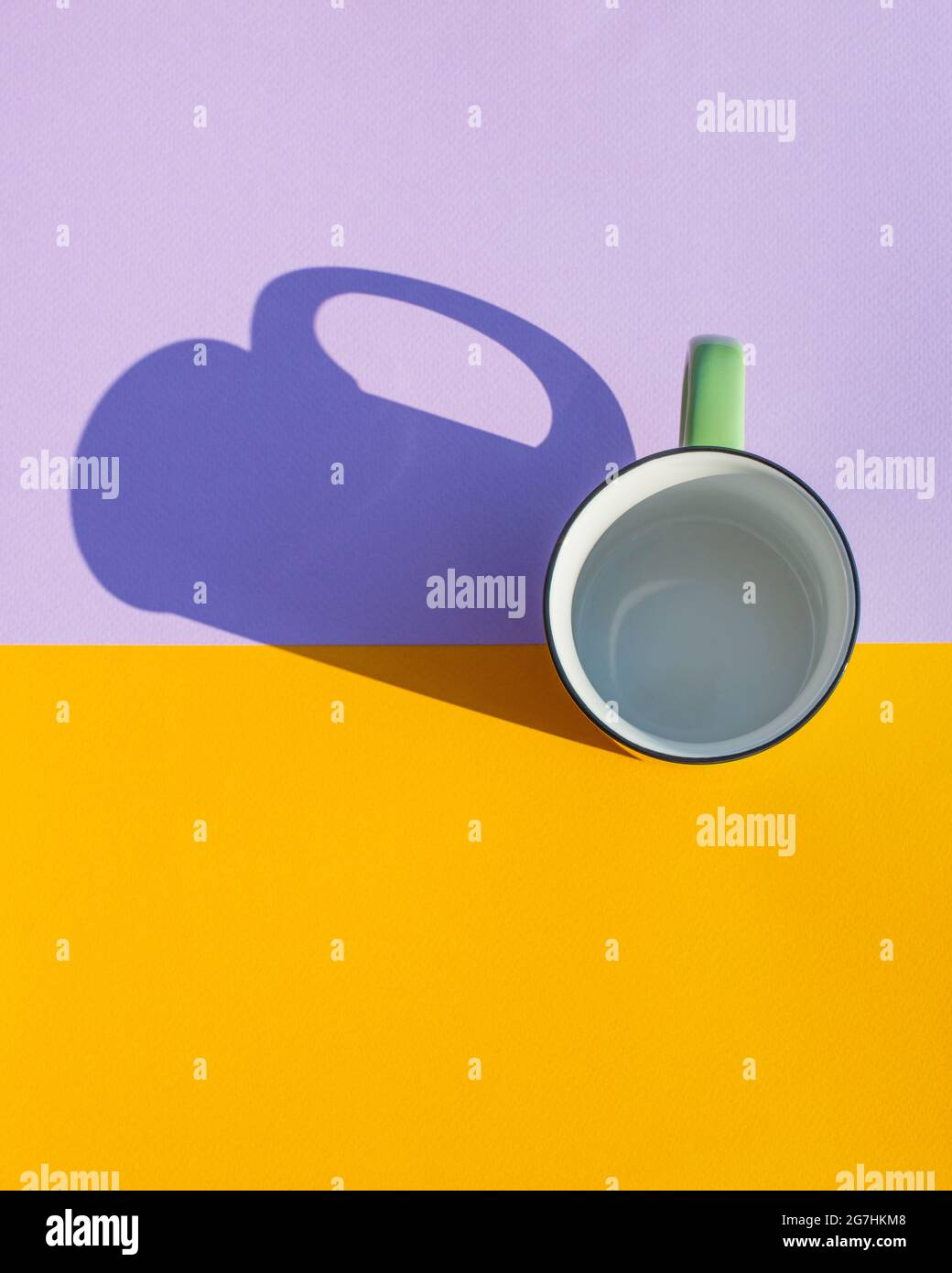 Un mug vert vide avec une ombre dure sur fond jaune et violet. Copier l'espace. Flat lay, vue de dessus. Banque D'Images