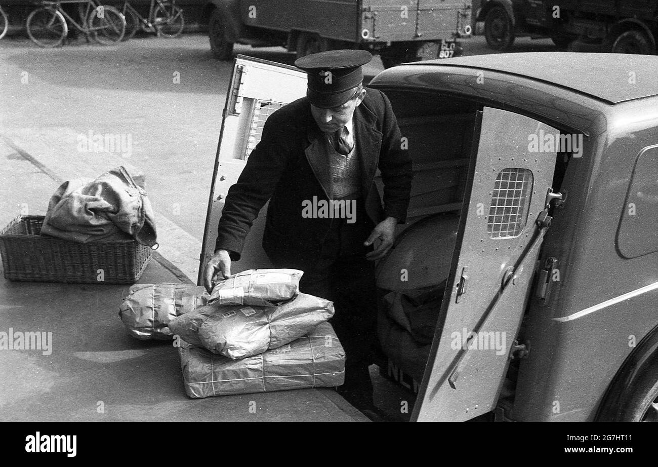 1950, historique, à l'extérieur de la cour d'un dépôt de courrier, un travailleur de GPO en uniforme avec des colis à charger dans l'arrière de son camion de livraison de poste, probablement un Morris Z, Londres, Angleterre, Royaume-Uni. Le constructeur automobile britannique Morris était actuellement le plus grand fournisseur de véhicules au General Post Office (GPO), le Morris Z étant le cheval de travail de la flotte, utilisé à la fois pour la livraison et la collecte. Le système postal du Royaume-Uni, le GPO, a été aboli en 1969 avec ses actifs transférés au bureau de poste, une société statutaire. Il est devenu Royal Mail Group PLC en 2002. Banque D'Images