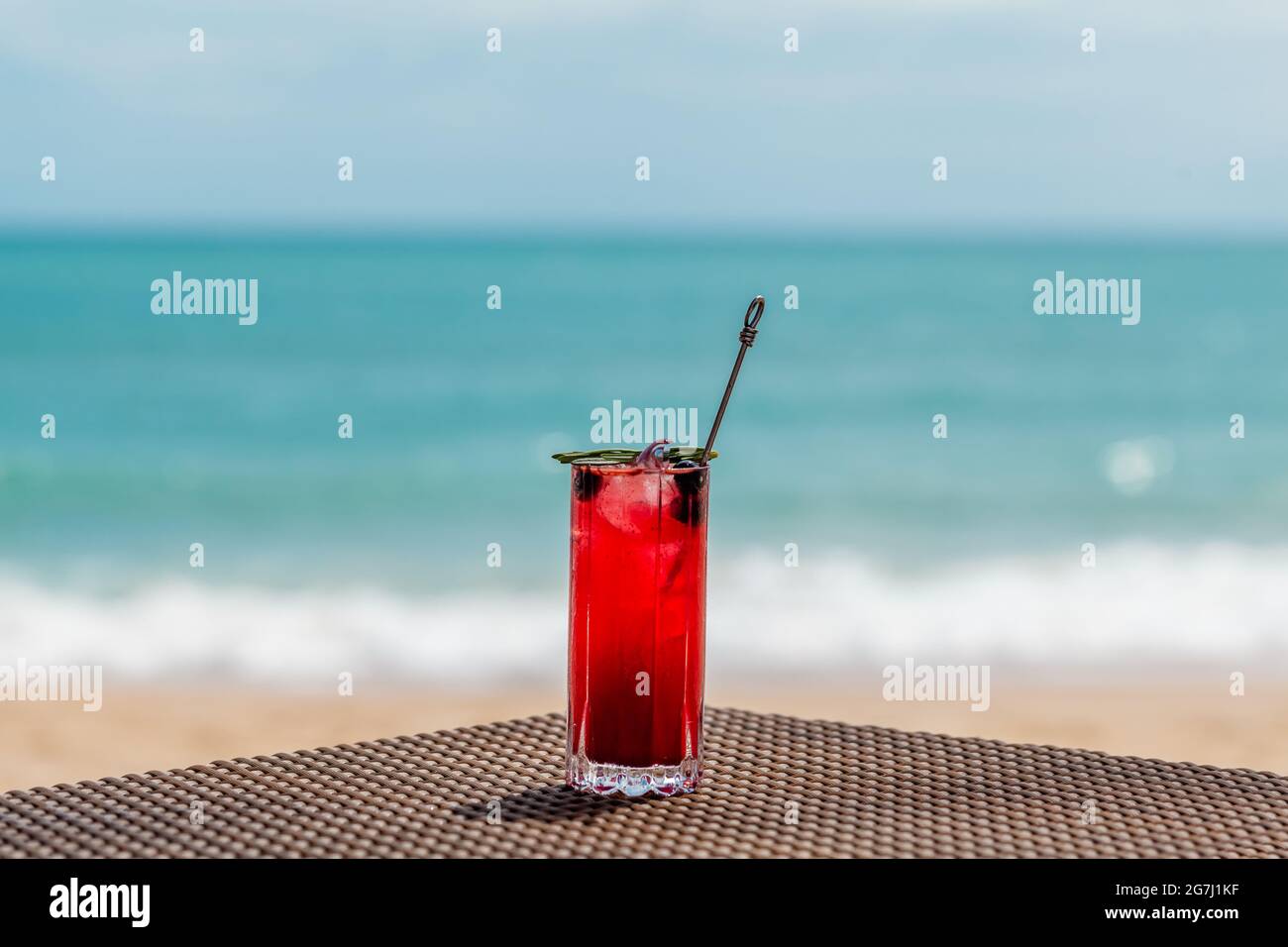Queue de macktail rouge froid avec baies sur la table de plage, vagues de mer défochies sur le fond Banque D'Images