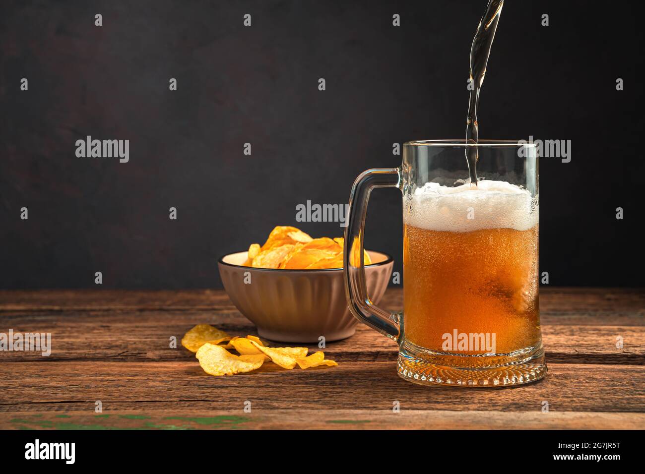 Verser de la bière mousseuse dans une tasse sur une table en bois avec des frites. Oktoberfest. Banque D'Images