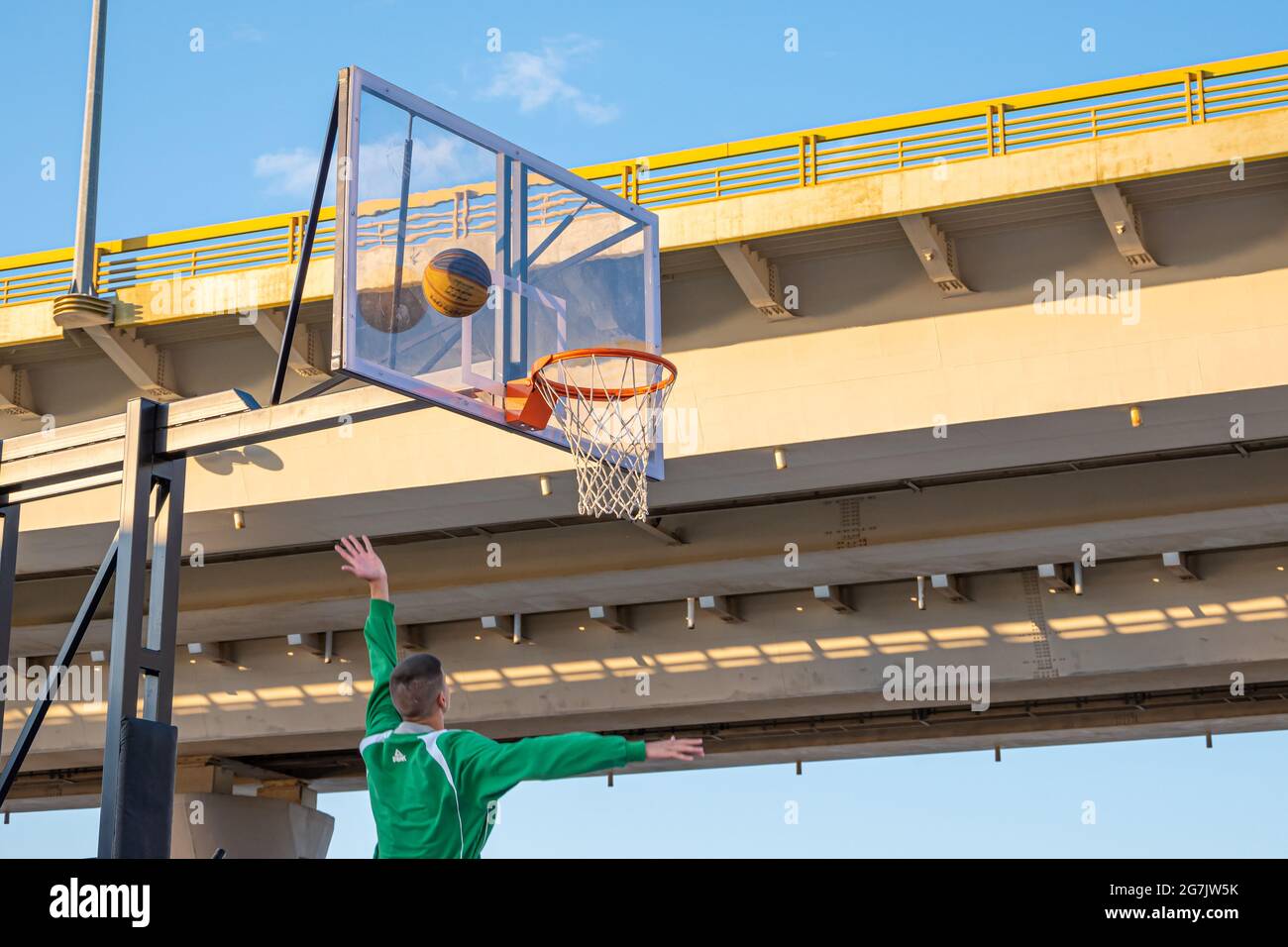 Kazan, Russie - 12 septembre 2020 : un jeune joueur de basket-ball jette une balle dans un panier de basket-ball contre le ciel bleu. Fond de panier en plastique transparent Banque D'Images