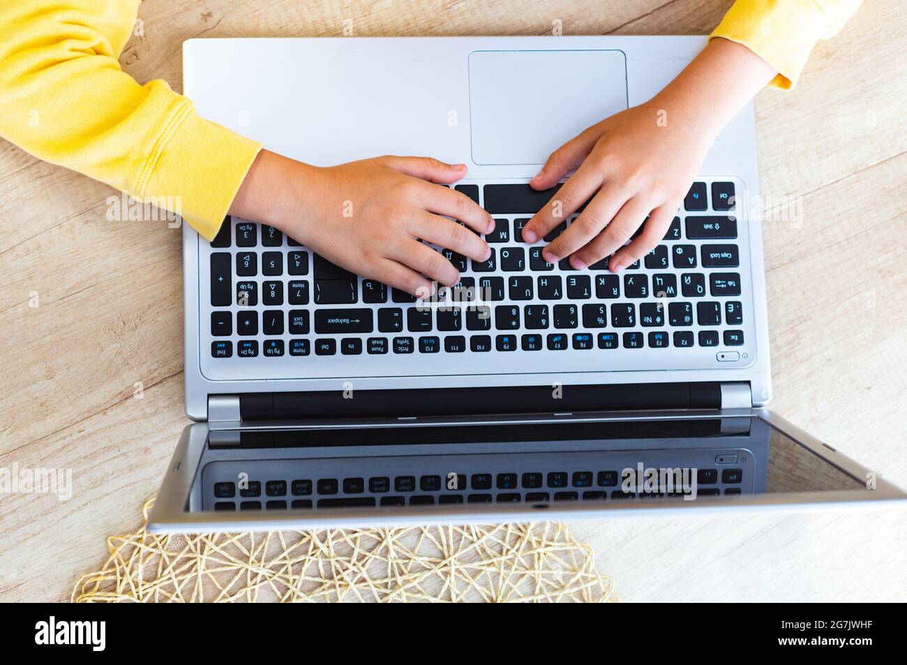 Les mains des enfants avec des manches jaunes sur un clavier d'ordinateur portable sur une table en bois clair, vue du dessus. Retour à l'école, homeschooling, e-learning. Social Banque D'Images